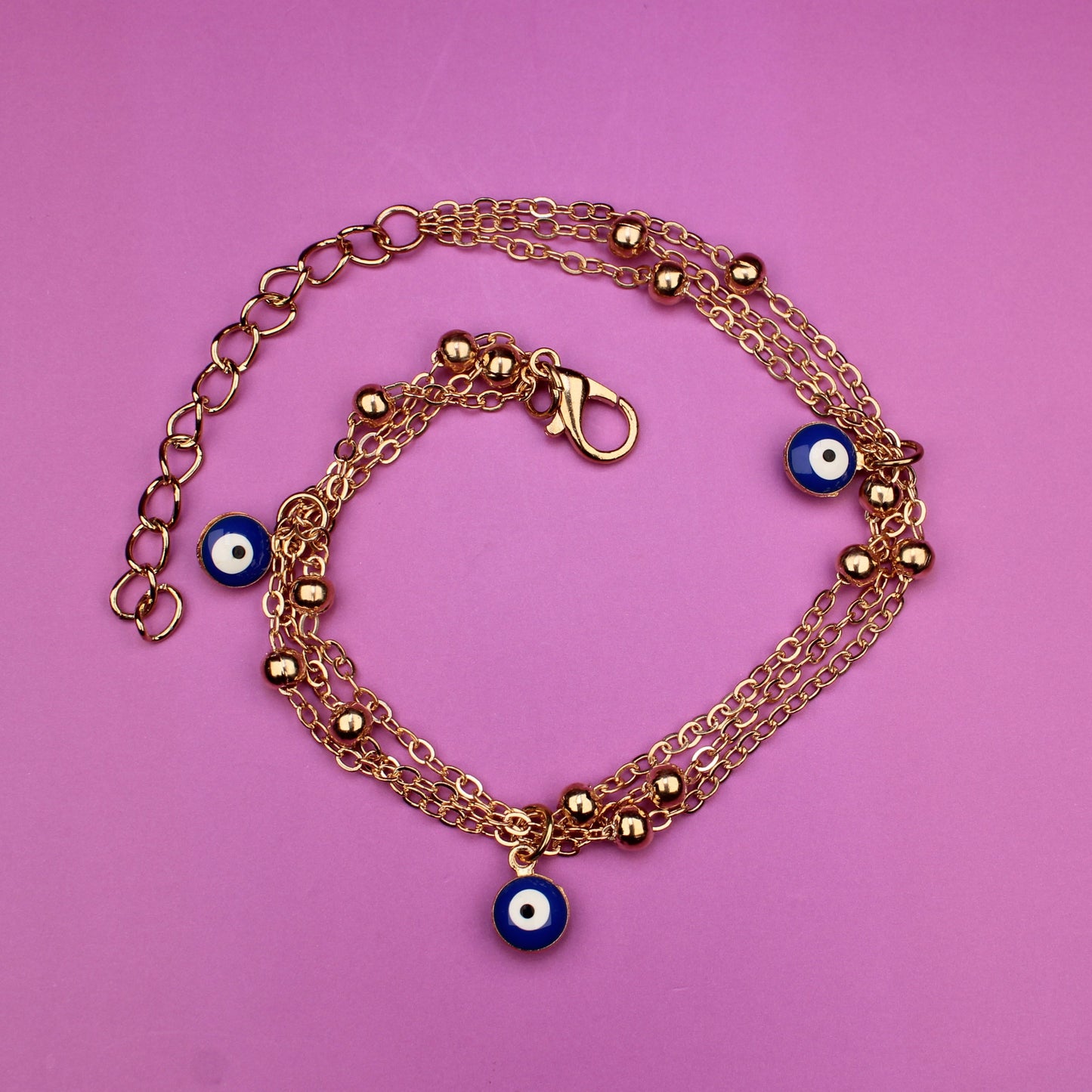 Gold bracelet with blue evil eye charms on a pink background