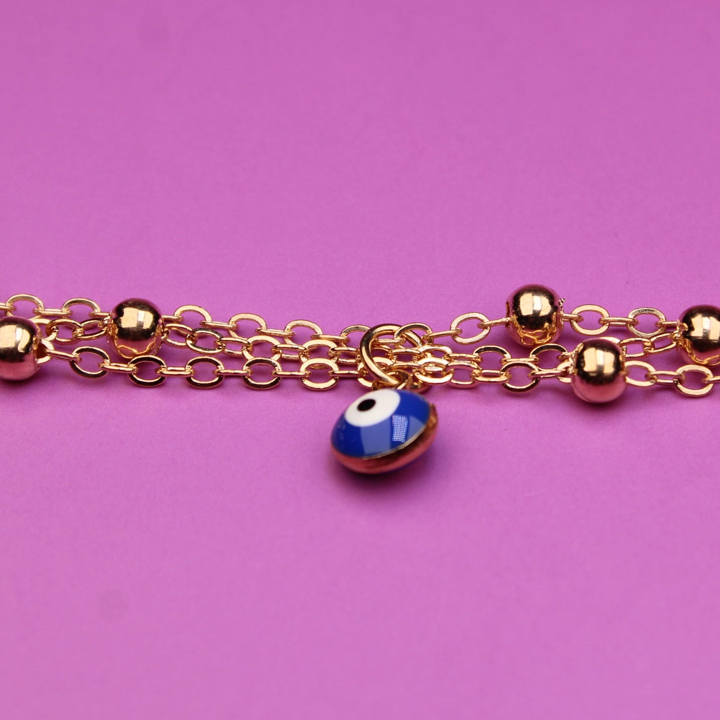 Gold bracelet with blue evil eye beads on a pink background