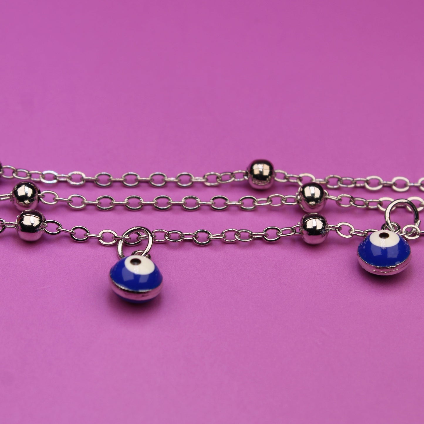 Silver chain bracelet with blue evil eye charms on a pink background