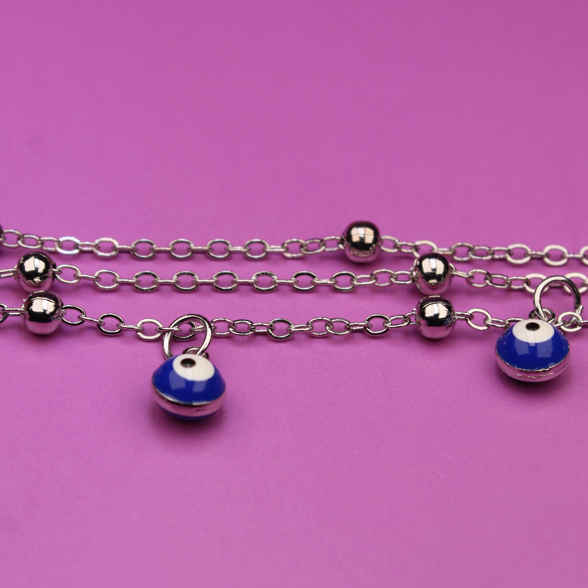Silver chain bracelet with blue evil eye charms on a pink background