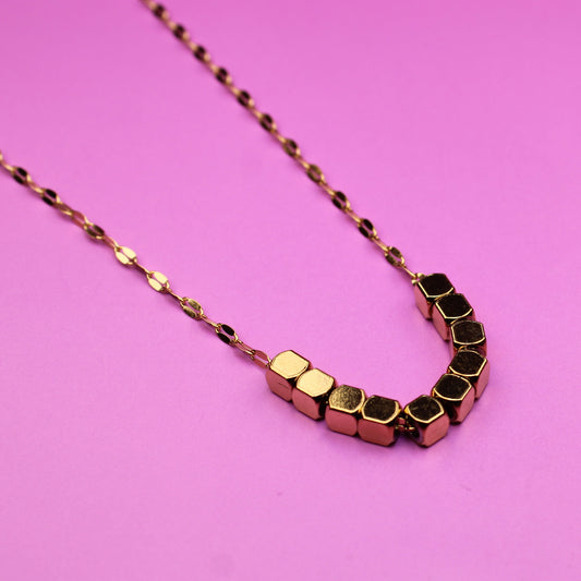Gold necklace with geometric beads on a pink background