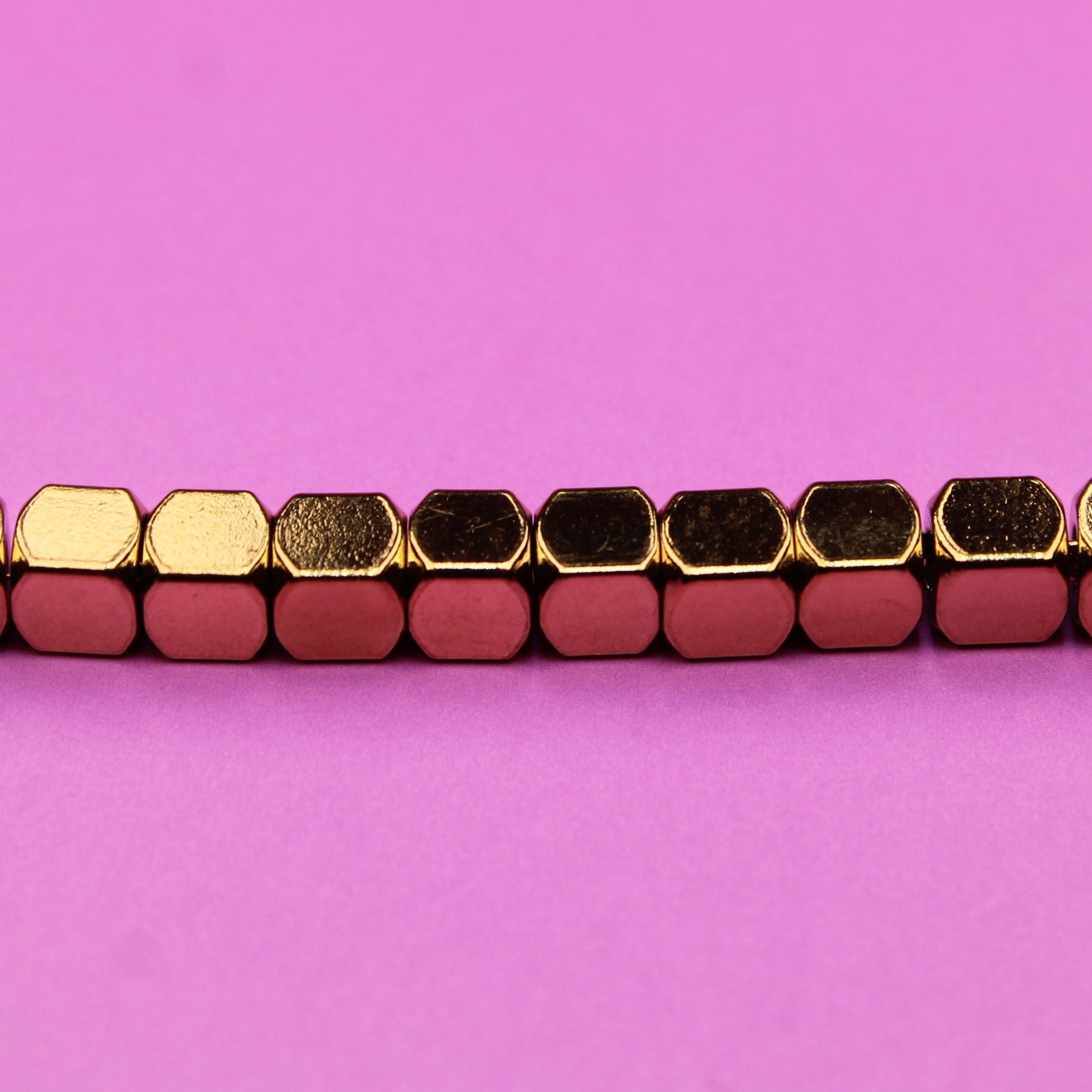 Bracelet with gold and red hexagonal beads on a pink background