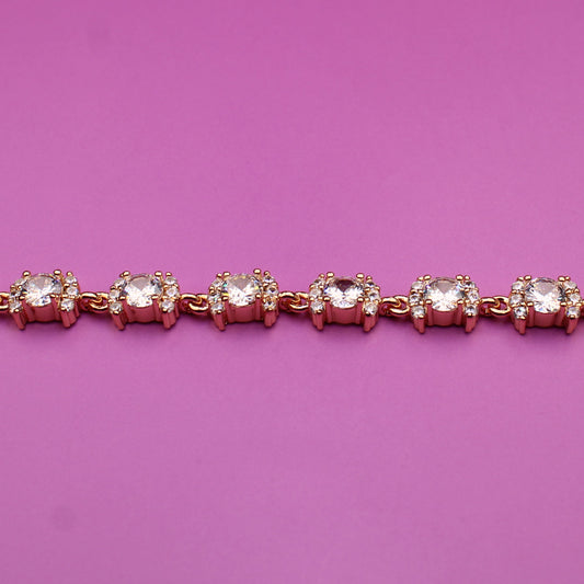 Rose gold bracelet with clear stones on a pink background