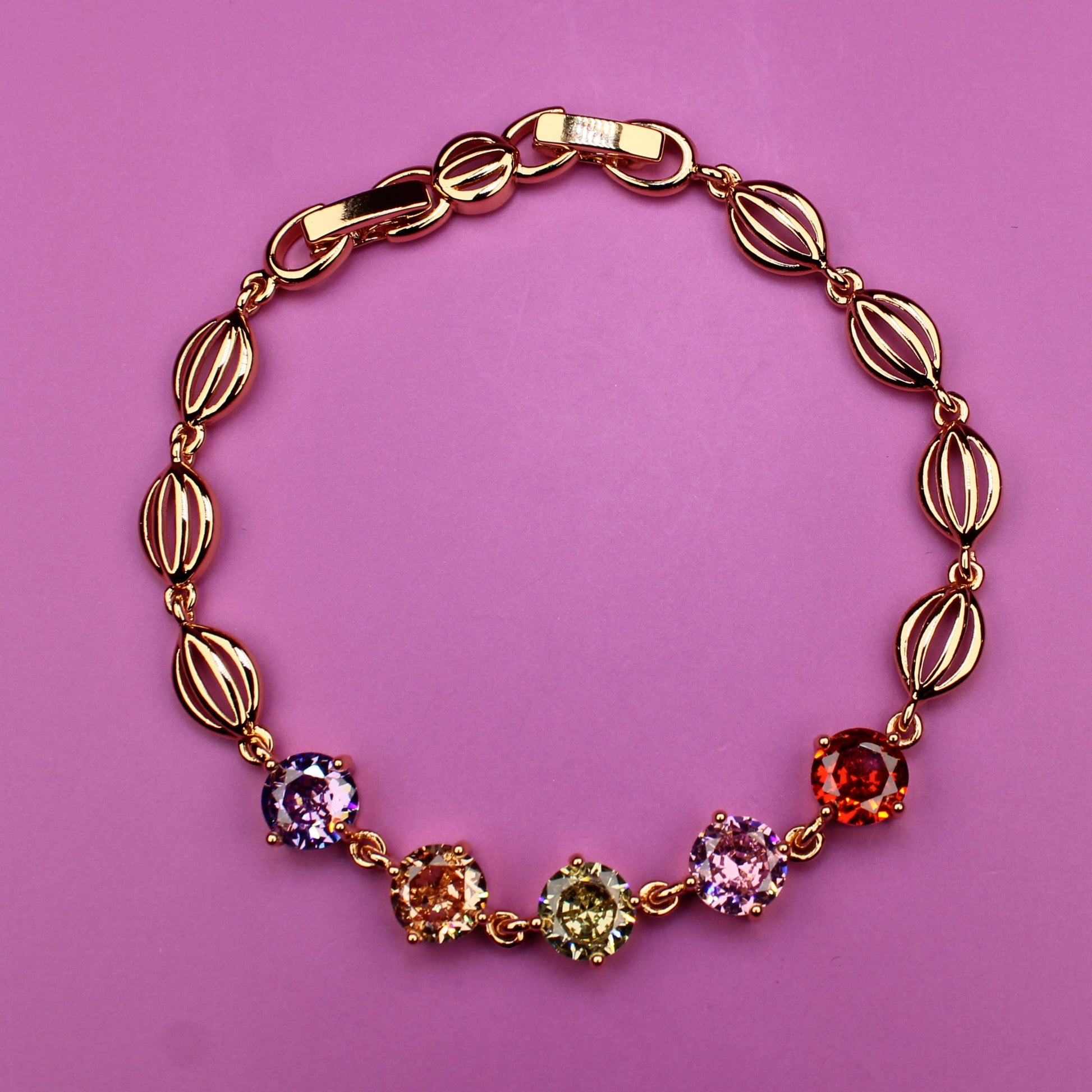 Gold bracelet with colorful gemstones on a pink background