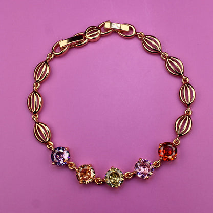 Gold bracelet with colorful gemstones on a pink background