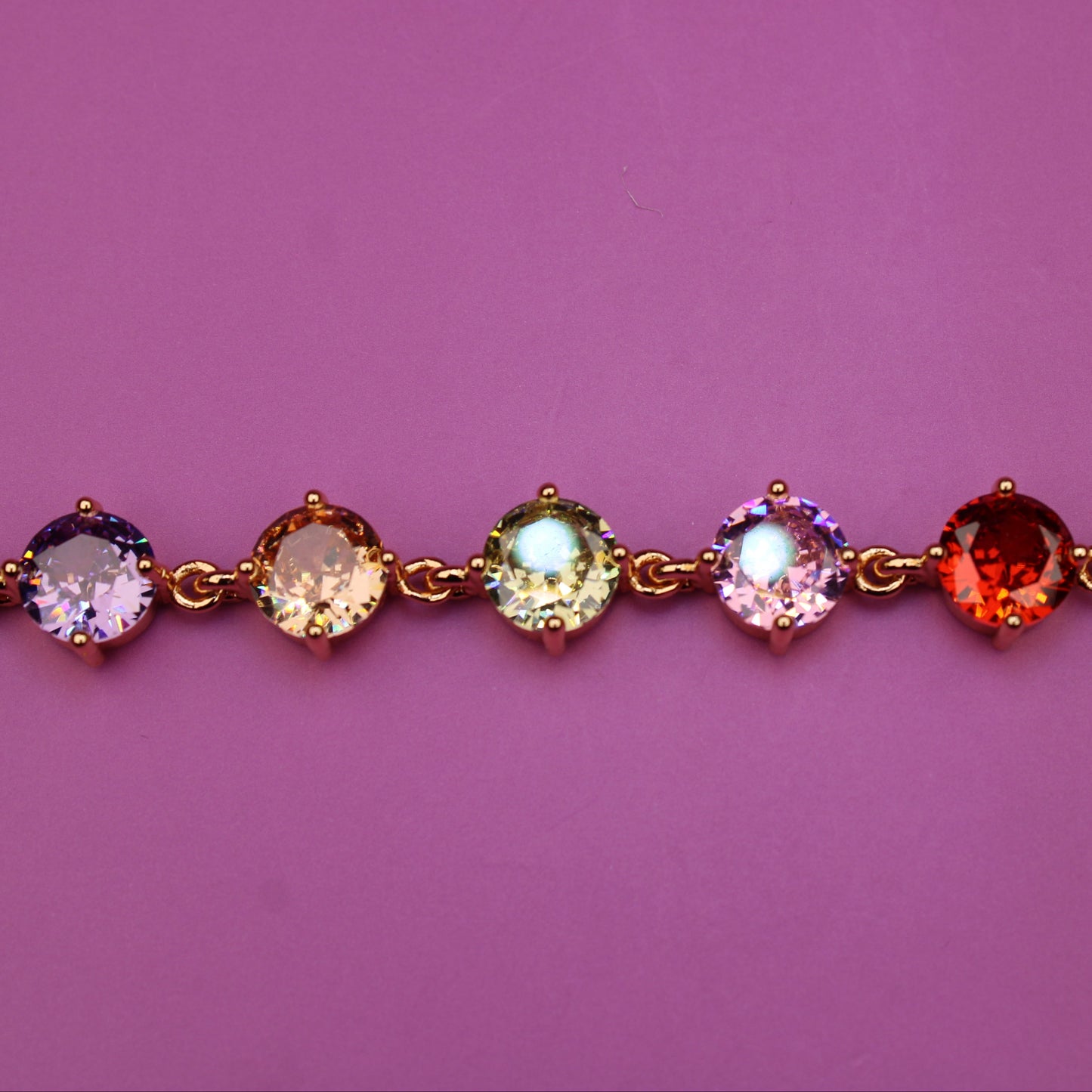 Gold bracelet with multicolored gemstones on a pink background