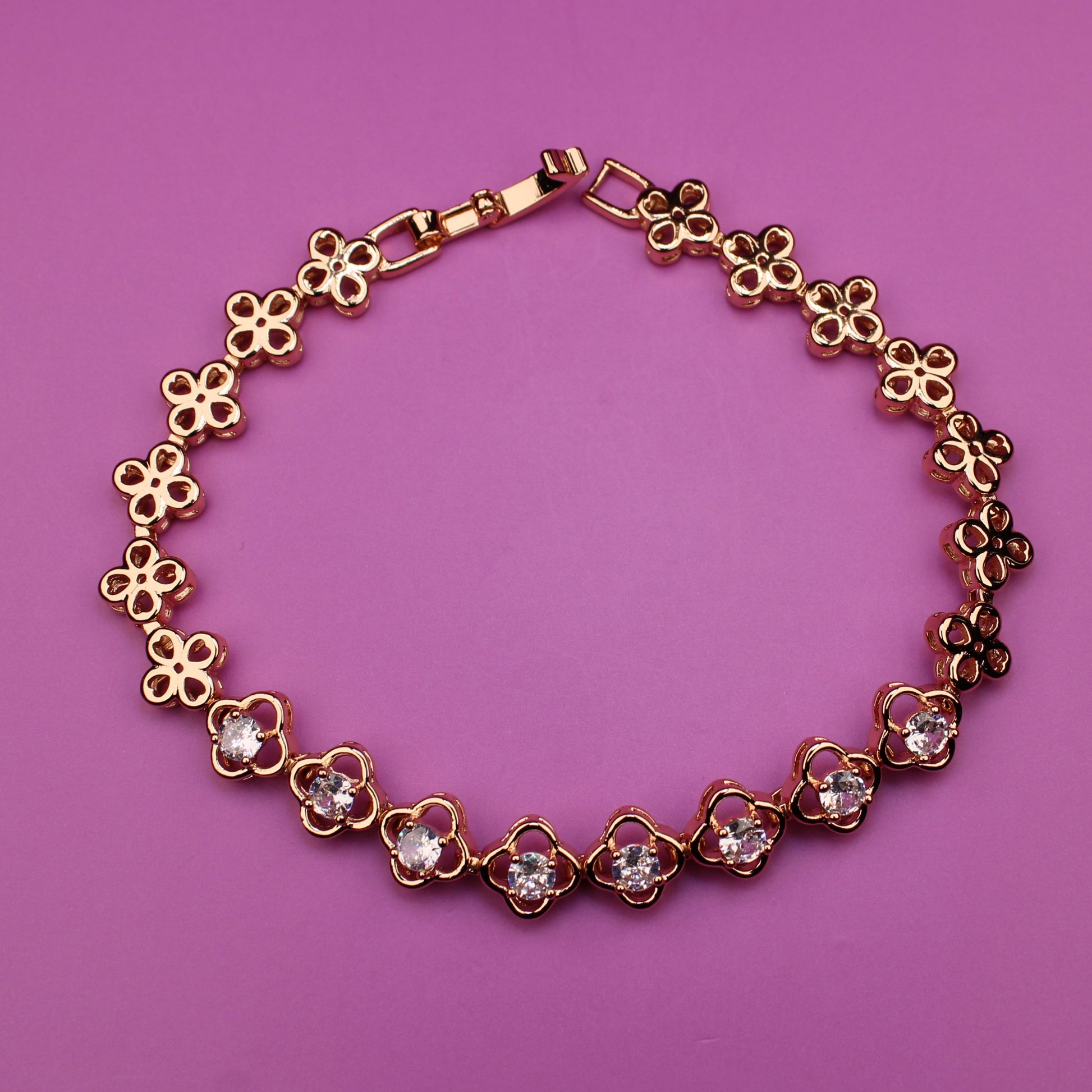 Gold bracelet with floral designs on a pink background