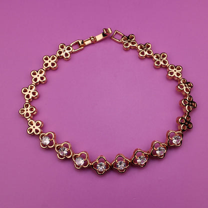 Gold bracelet with floral designs on a pink background