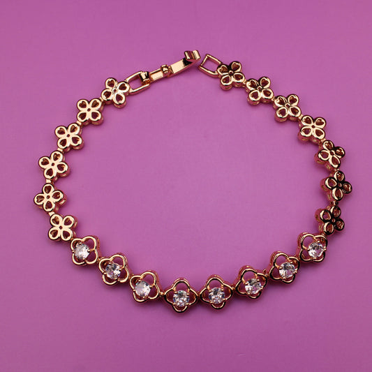 Gold bracelet with floral designs on a pink background