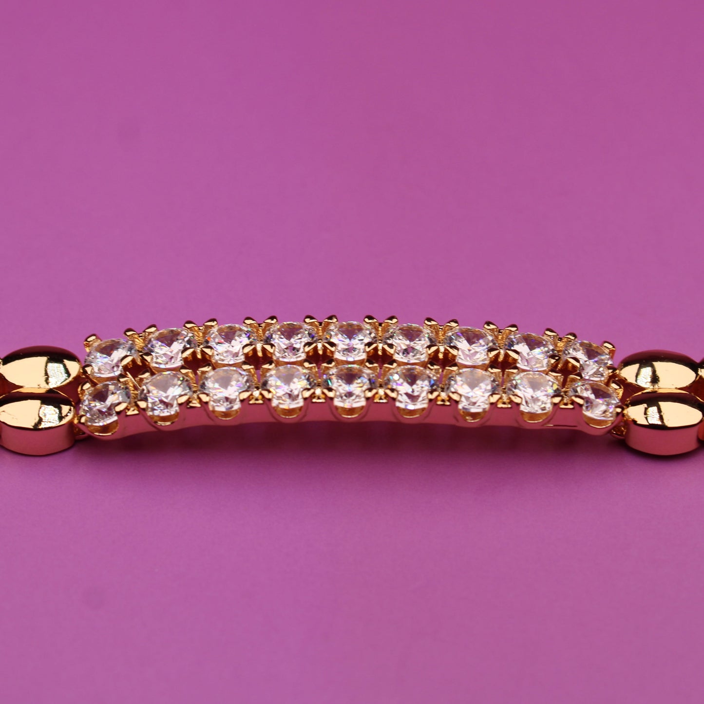 Gold bracelet with a diamond clasp on a pink background