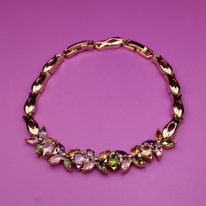 Gold bracelet with colorful gemstones on a pink background