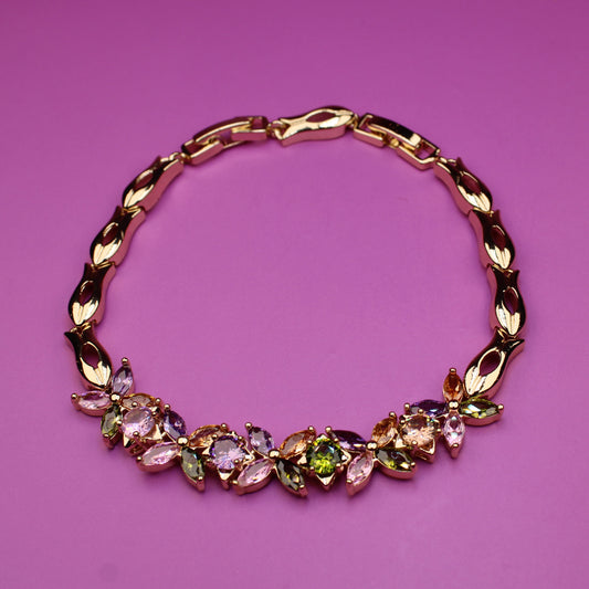 Gold bracelet with colorful gemstones on a pink background