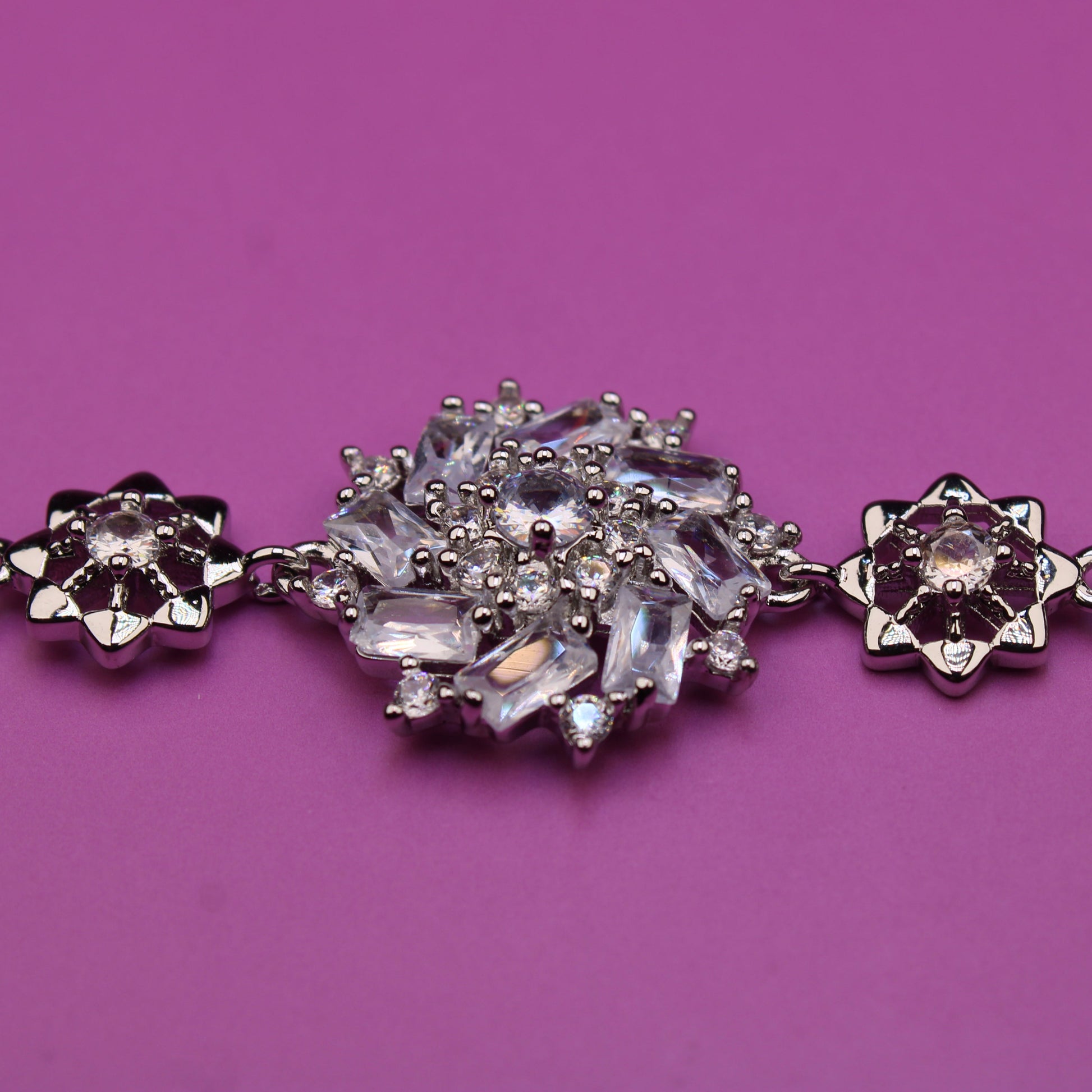 Silver bracelet with floral designs and clear stones on a purple background