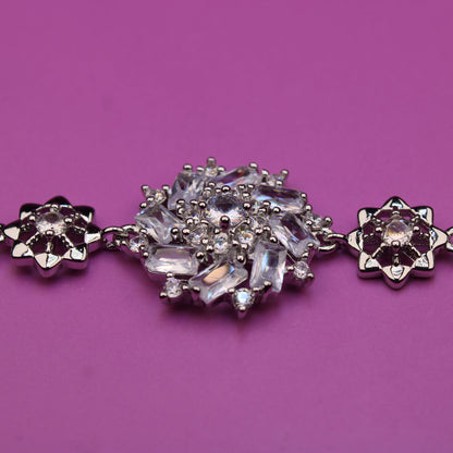 Silver bracelet with floral designs and clear stones on a purple background