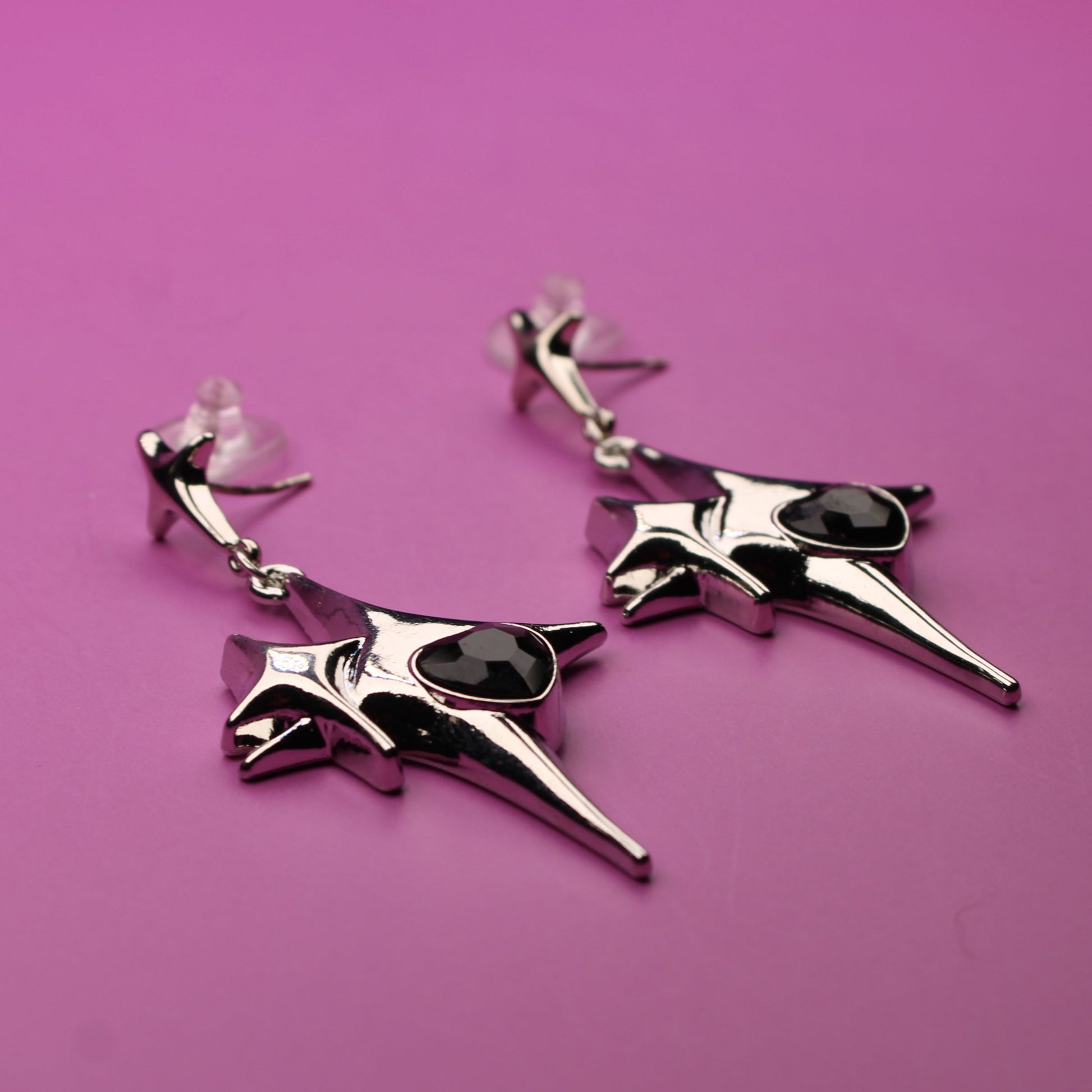 Pair of silver earrings with black stones on a pink background