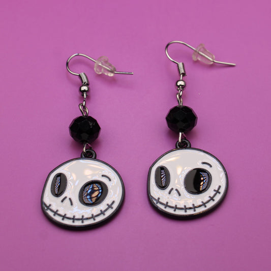 Pair of skeleton face earrings on a pink background