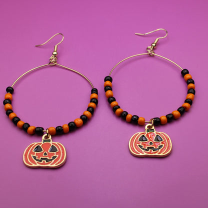 Halloween-themed hoop earrings with pumpkin charms on a purple background
