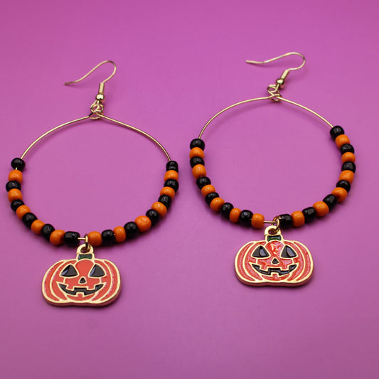 Halloween-themed hoop earrings with pumpkin charms on a purple background