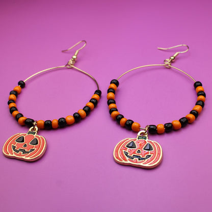 Halloween-themed beaded hoop earrings with pumpkin charms on a purple background