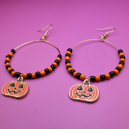 Halloween-themed beaded hoop earrings with pumpkin charms on a purple background