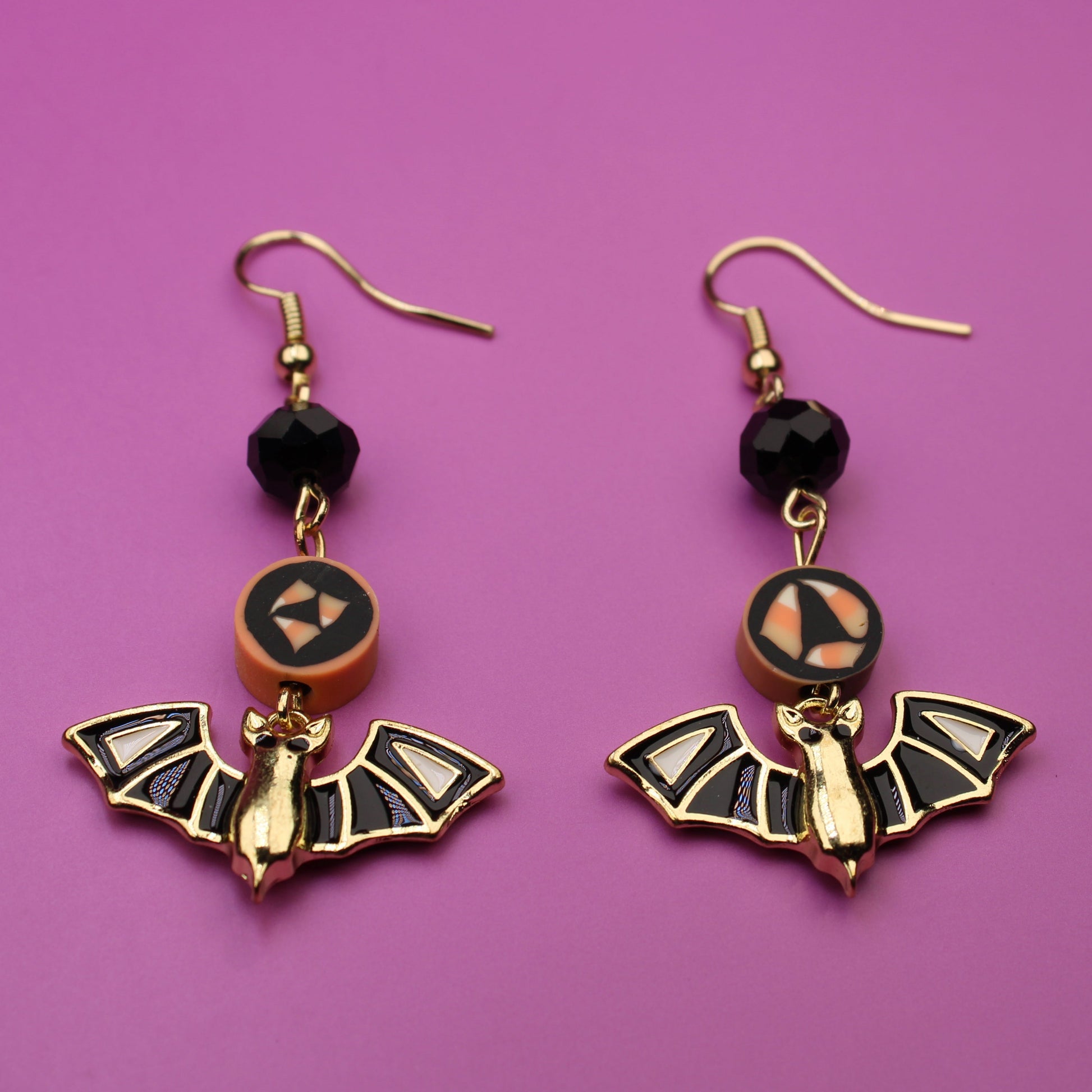 Bat-shaped earrings with black beads on a purple background
