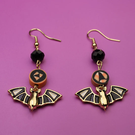 Bat-shaped earrings with black beads on a purple background