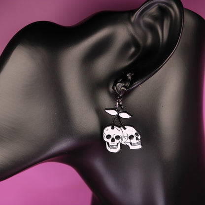 Skull-themed earrings on a black mannequin ear against a pink background