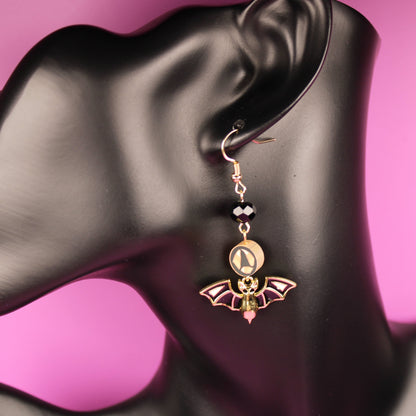 Bat-shaped earring on a black mannequin ear with a pink background