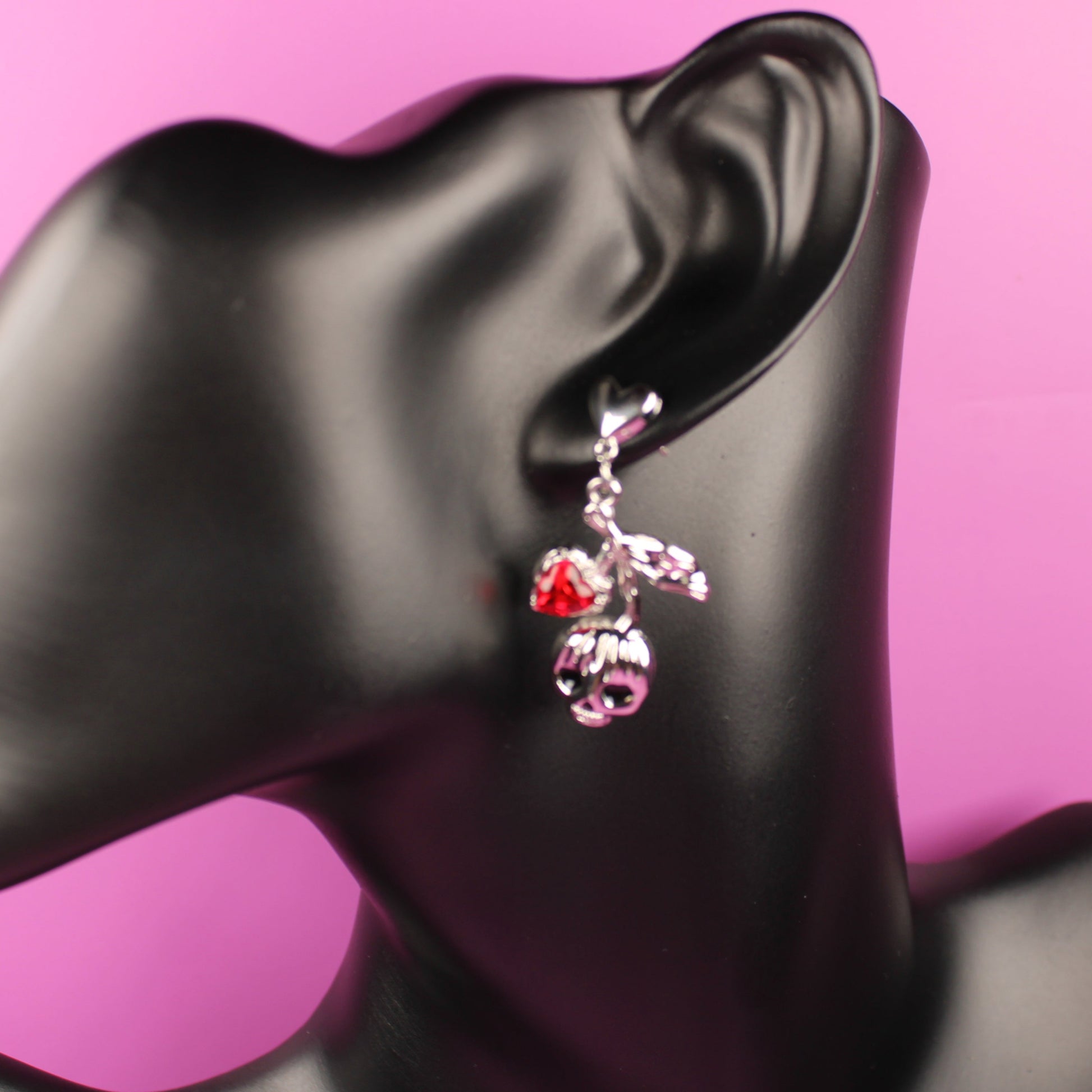 Earring on a black mannequin ear against a pink background
