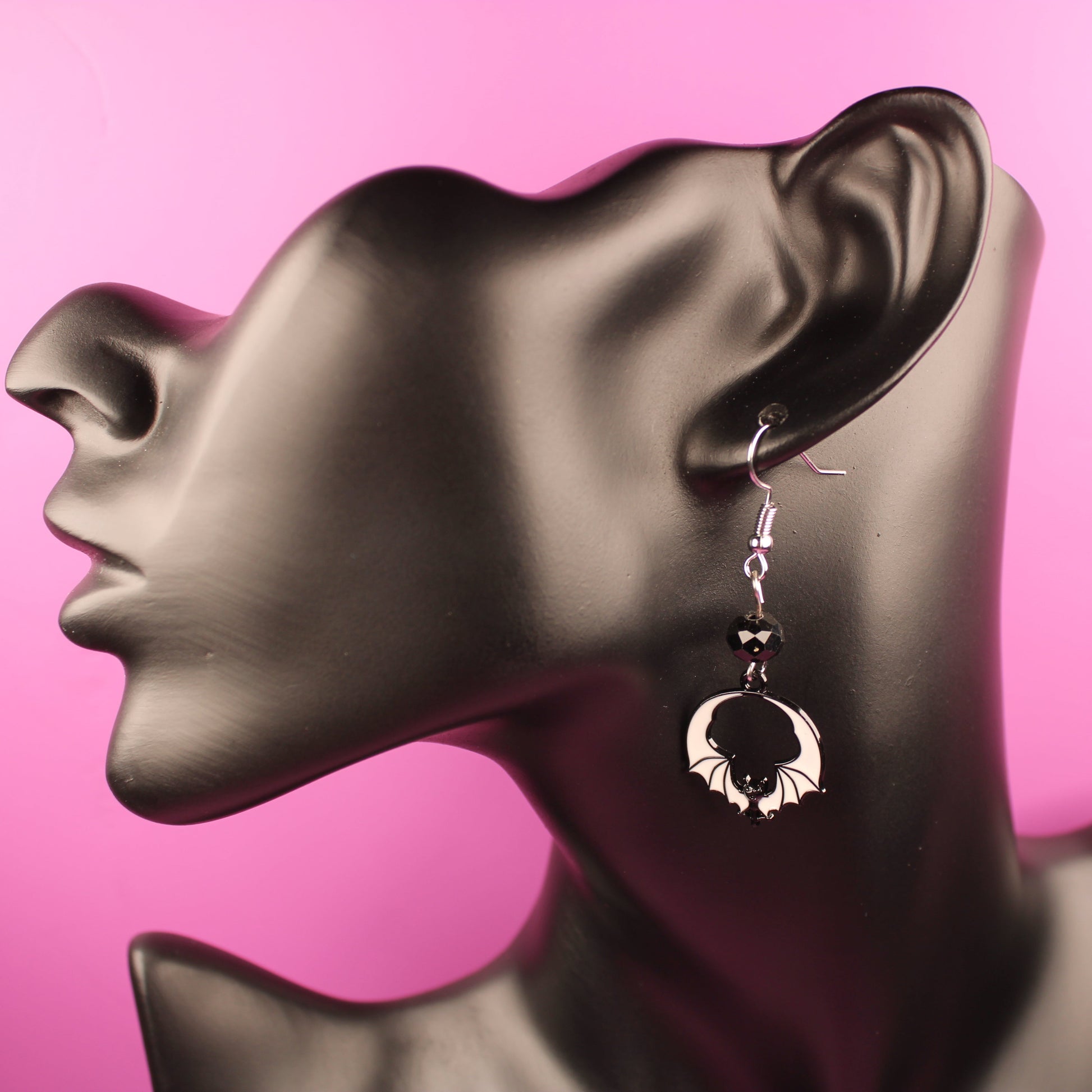 Earring on a mannequin ear against a pink background