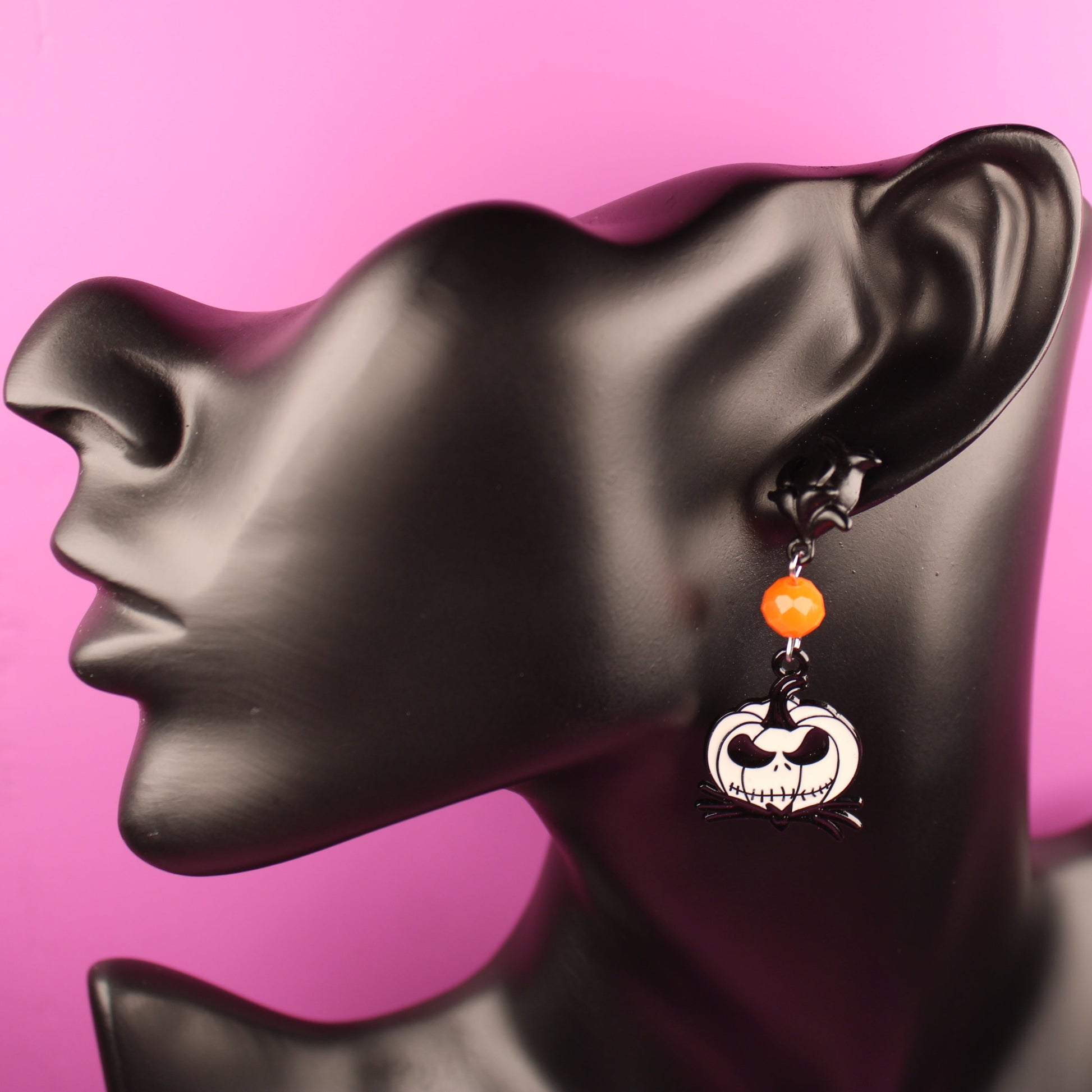 Halloween-themed earrings on a black mannequin head against a pink background