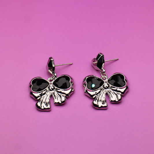 Pair of black bow-shaped earrings on a pink background