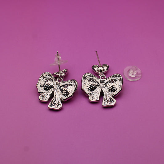Silver bow-shaped earrings on a pink background