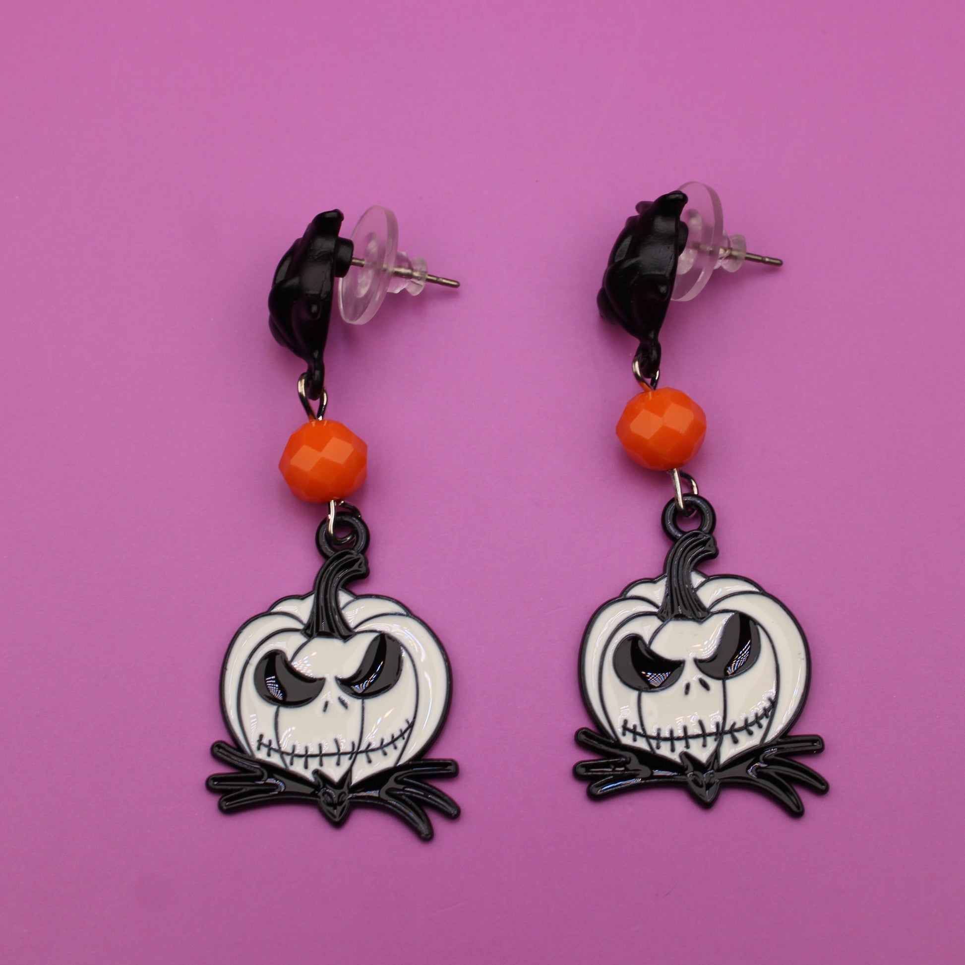 Pair of earrings with skull design on a pink background