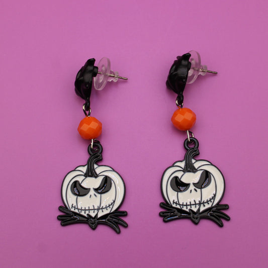 Pair of earrings with skull design on a pink background