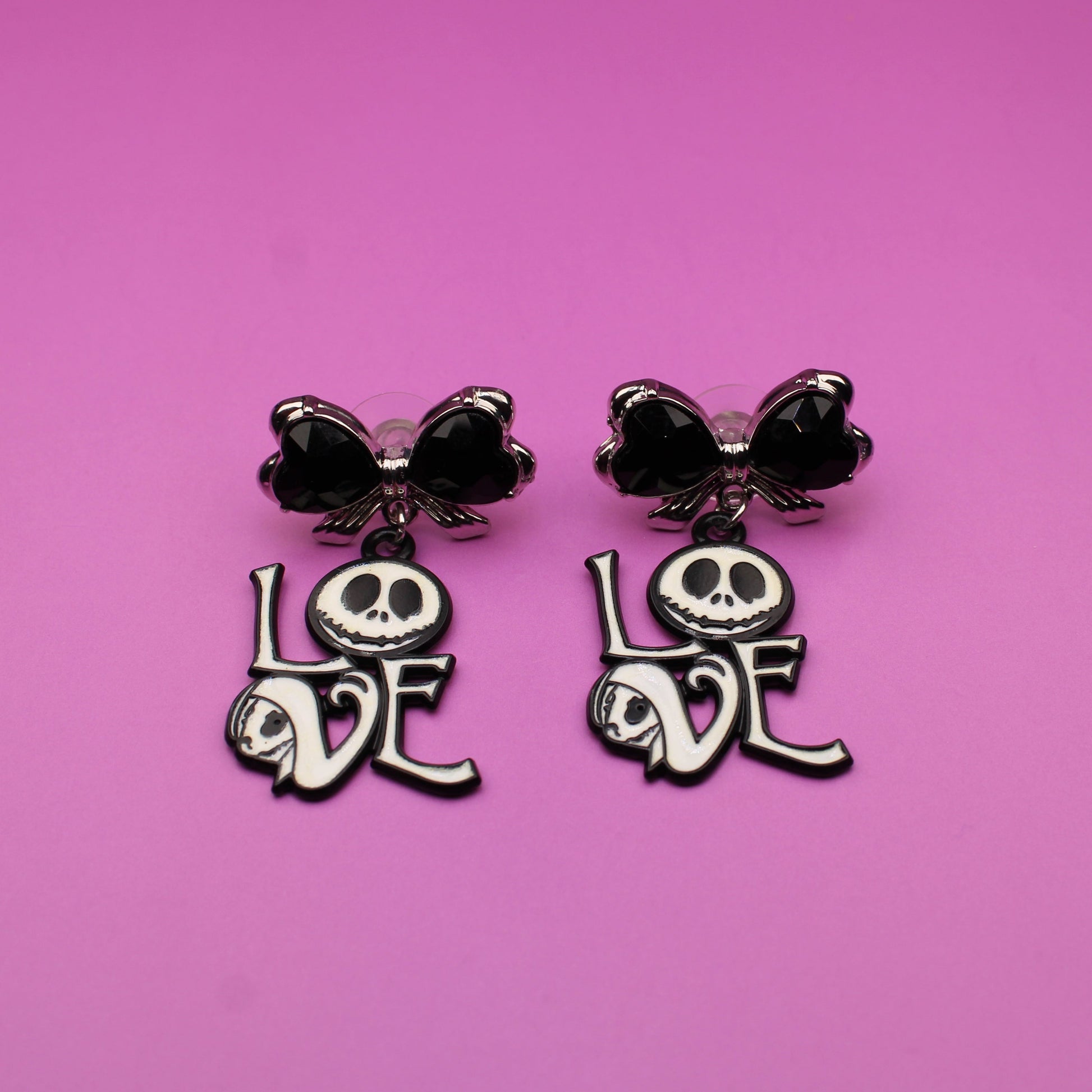 Pair of earrings with skull designs and 'LOVE' text on a pink background