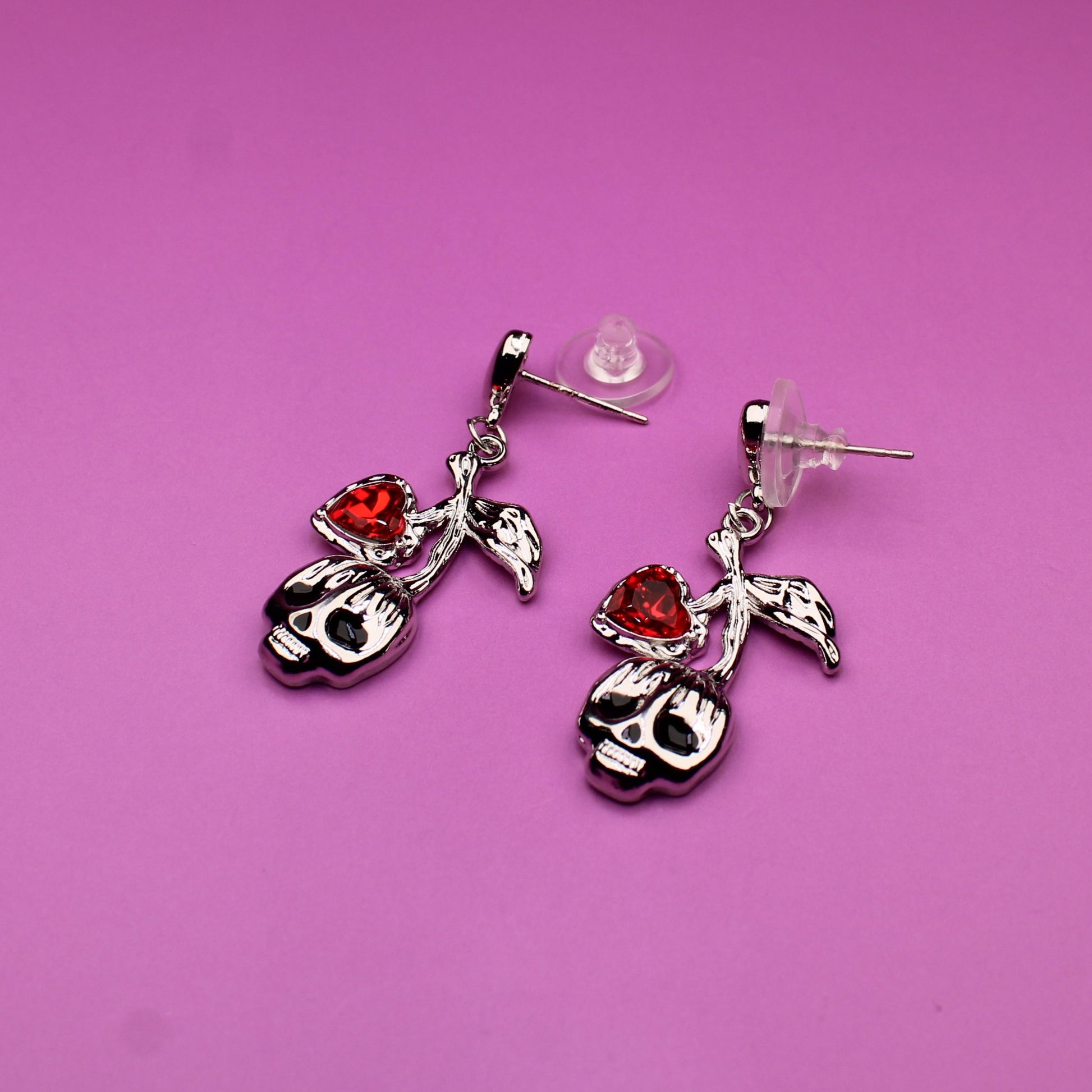 Pair of earrings with skull designs on a pink background