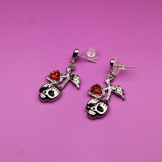Pair of earrings with skull designs on a pink background
