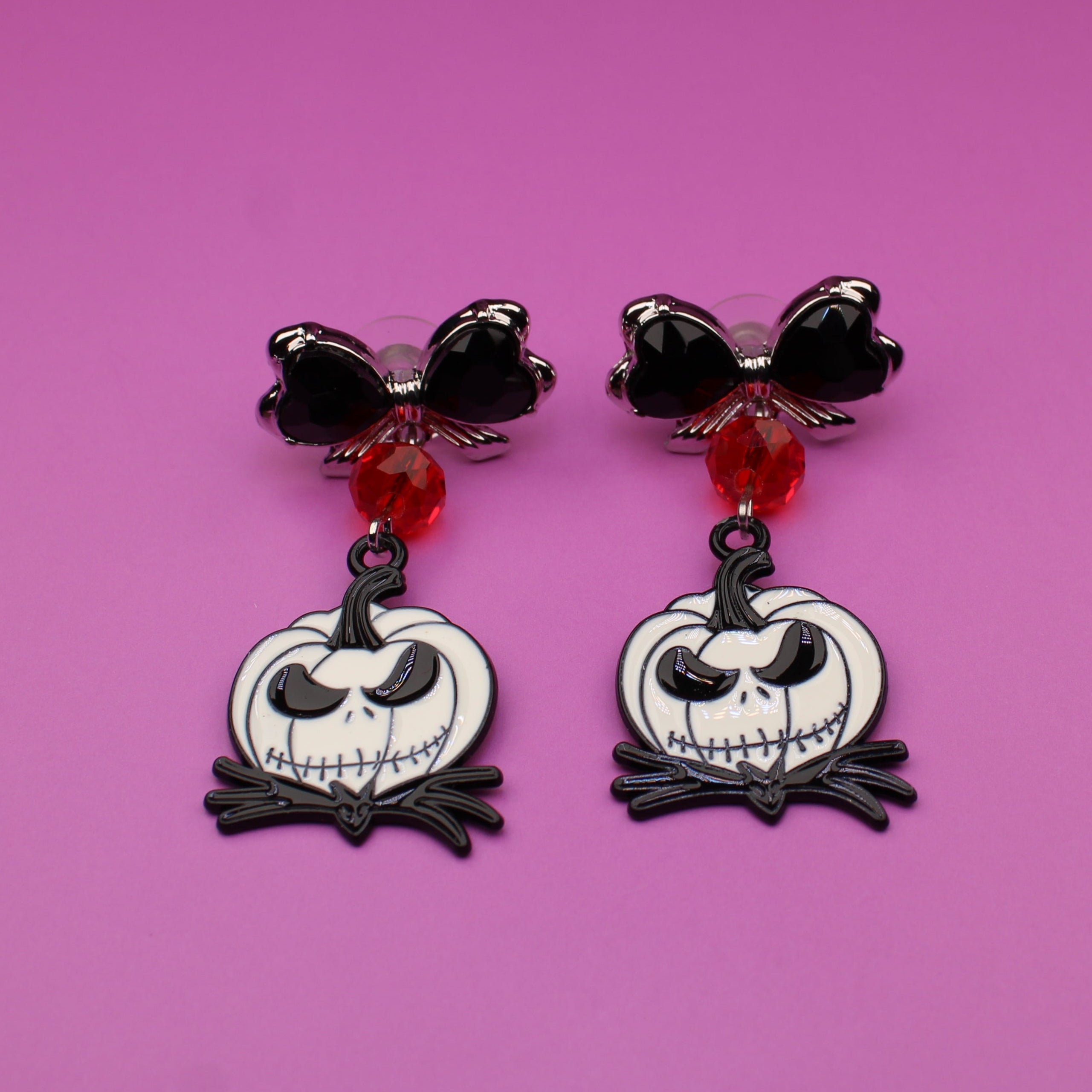 Pair of Halloween-themed earrings with jack-o'-lantern design on a pink background
