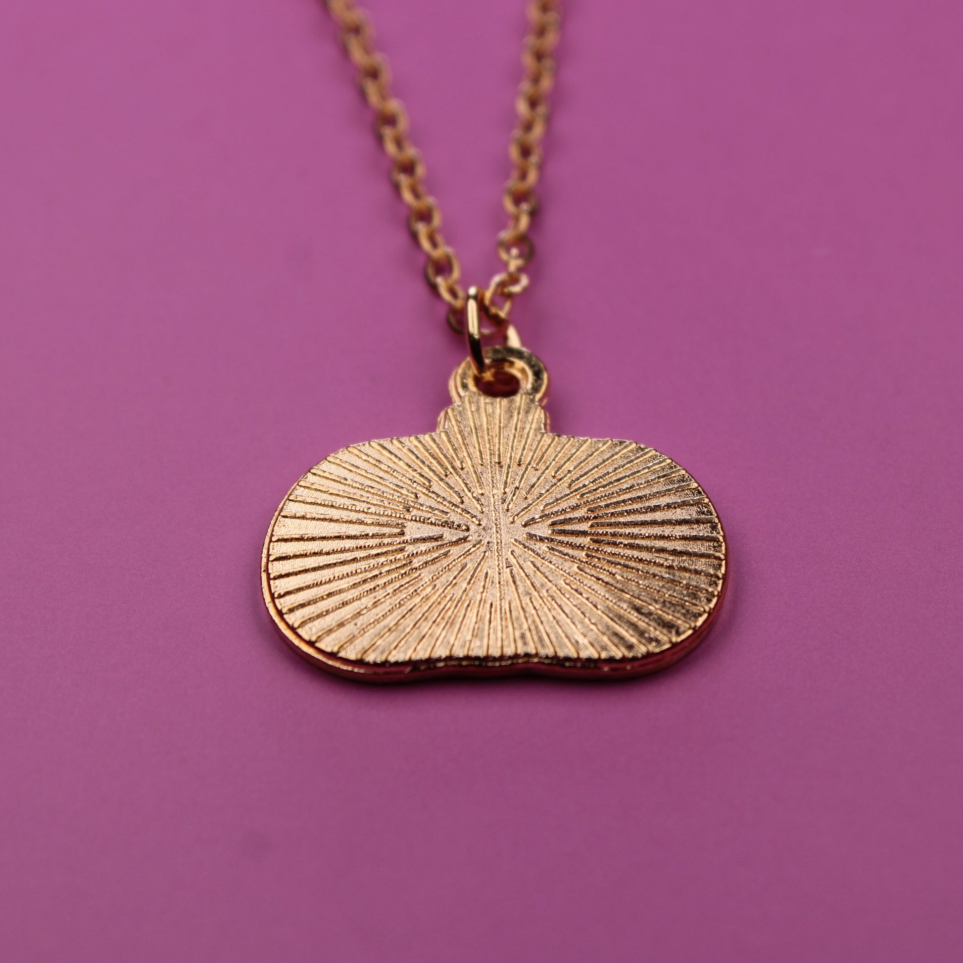 Gold necklace with a sunburst pendant on a purple background