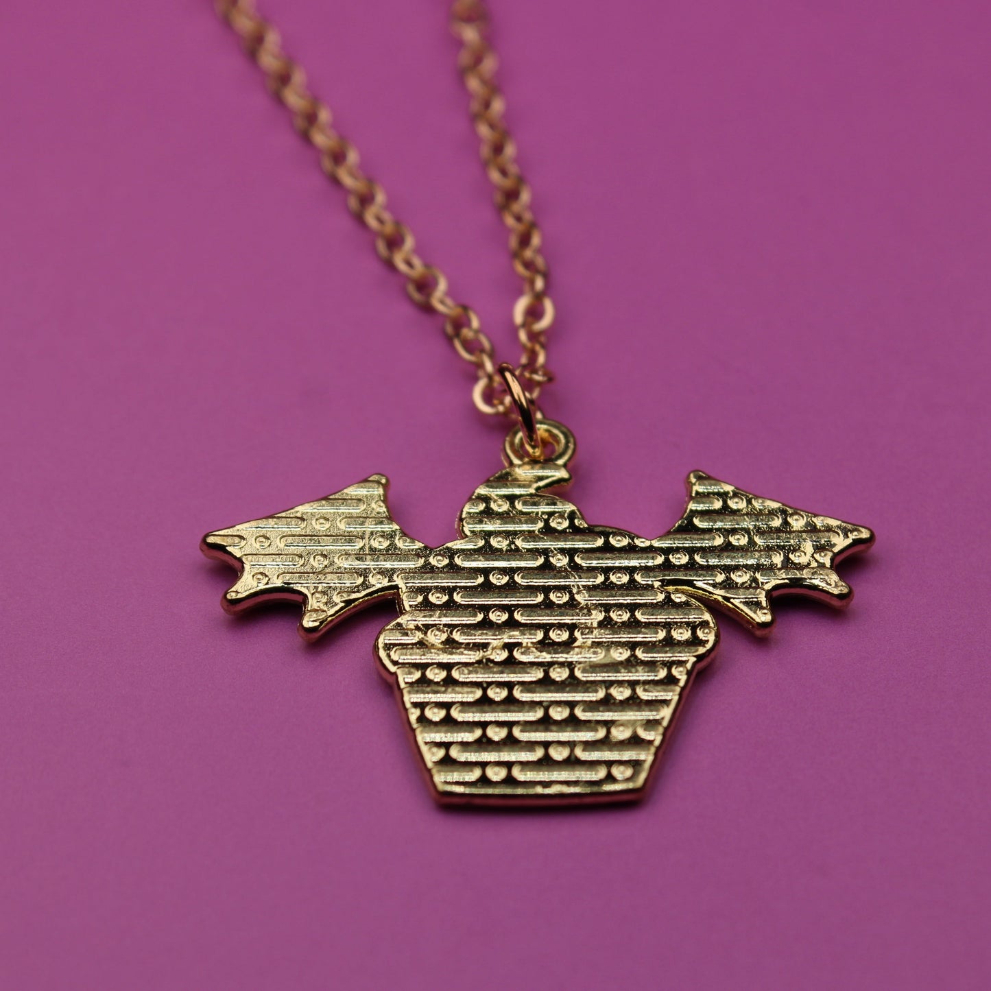 Gold necklace with a textured pendant on a purple background