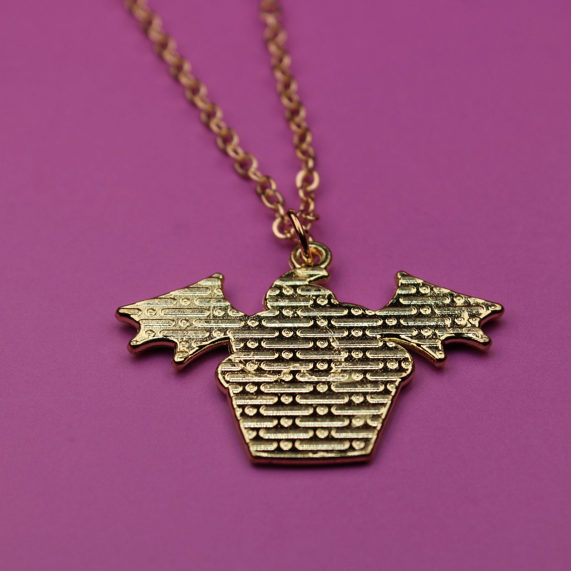 Gold necklace with a textured pendant on a purple background