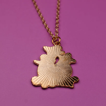Gold necklace with a leaf-shaped pendant on a purple background