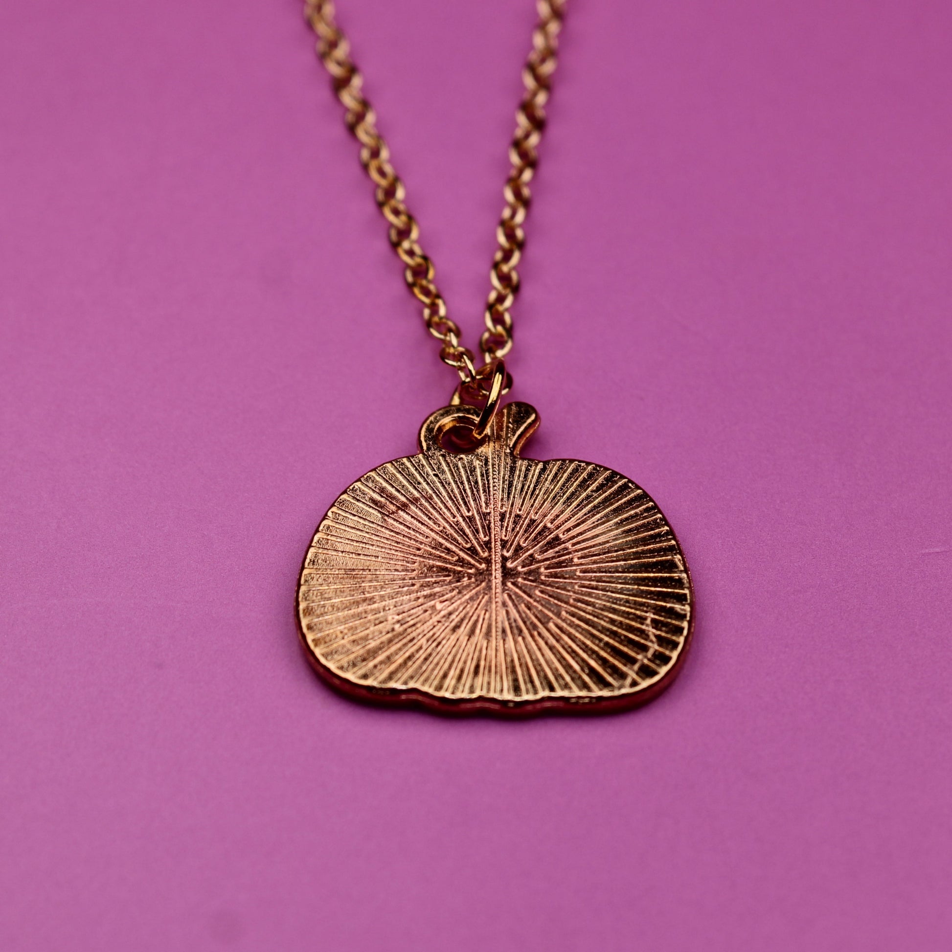 Gold necklace with a circular pendant on a pink background