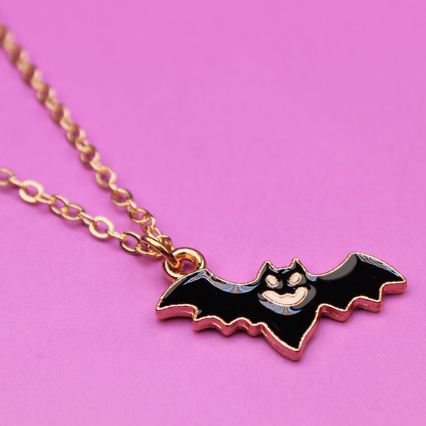 Bat-shaped pendant on a chain against a pink background