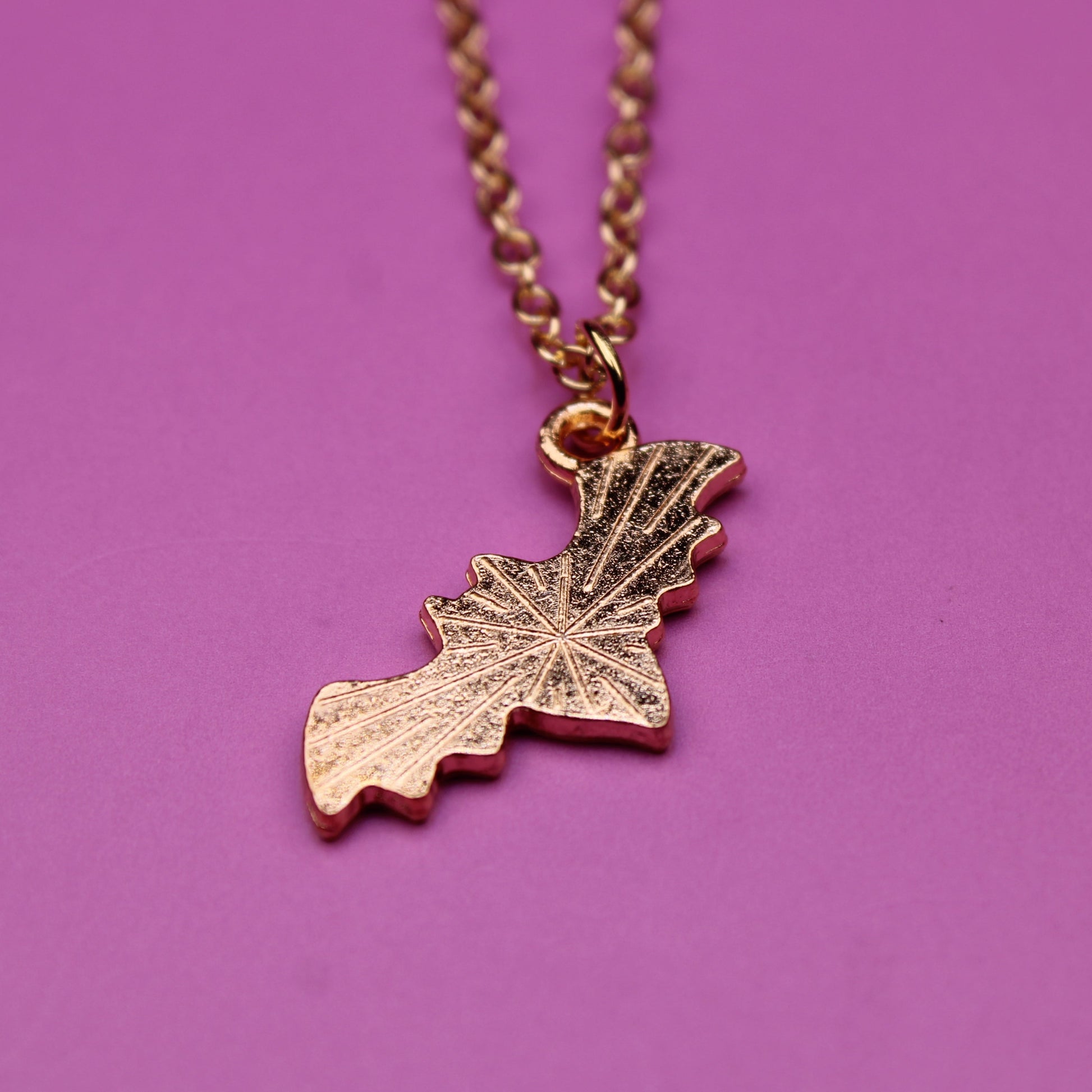 Gold leaf-shaped pendant on a chain against a purple background