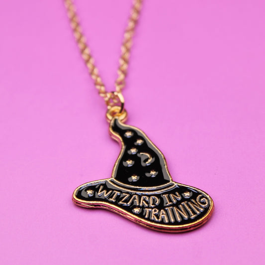 Necklace with a witch hat pendant labeled 'Wizard in Training' on a pink background