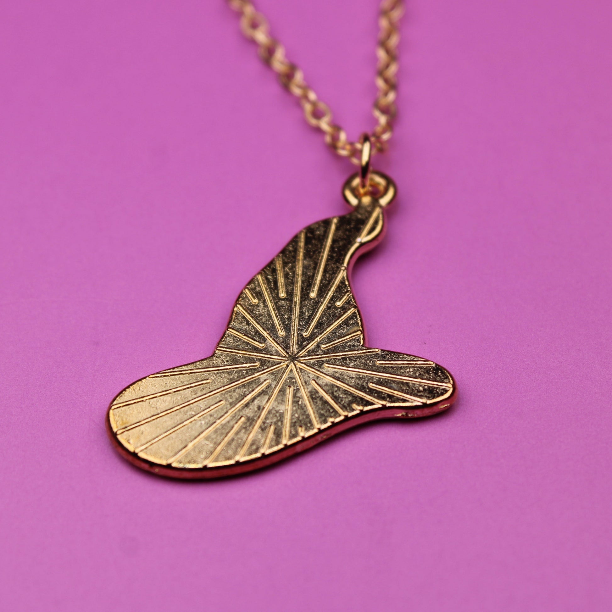 Gold leaf-shaped pendant on a chain against a pink background