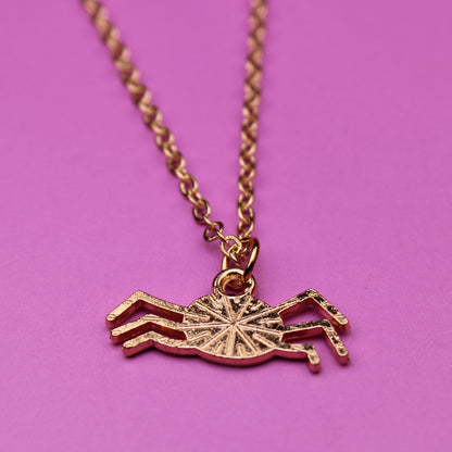 Gold crab-shaped pendant on a chain against a pink background