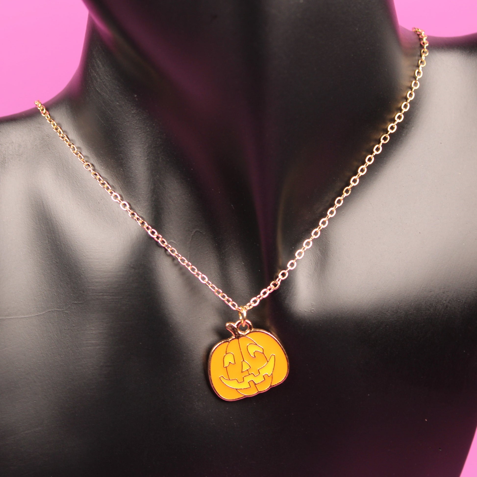 Gold necklace with a yellow pendant on a black mannequin bust against a pink background